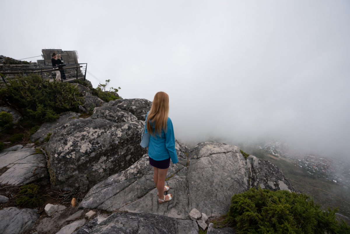 Misty scenery from the top of Table Mountain, with a lone visitor gazing into the clouds, representing the tranquil escape nature provides in Cape Town.