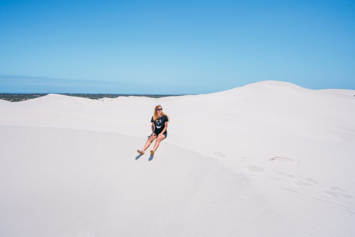 A lone traveler sitting on the pristine white sands of the Atlantis Dunes in South Africa, a serene and expansive landscape ideal for visitors seeking tranquility and natural beauty.