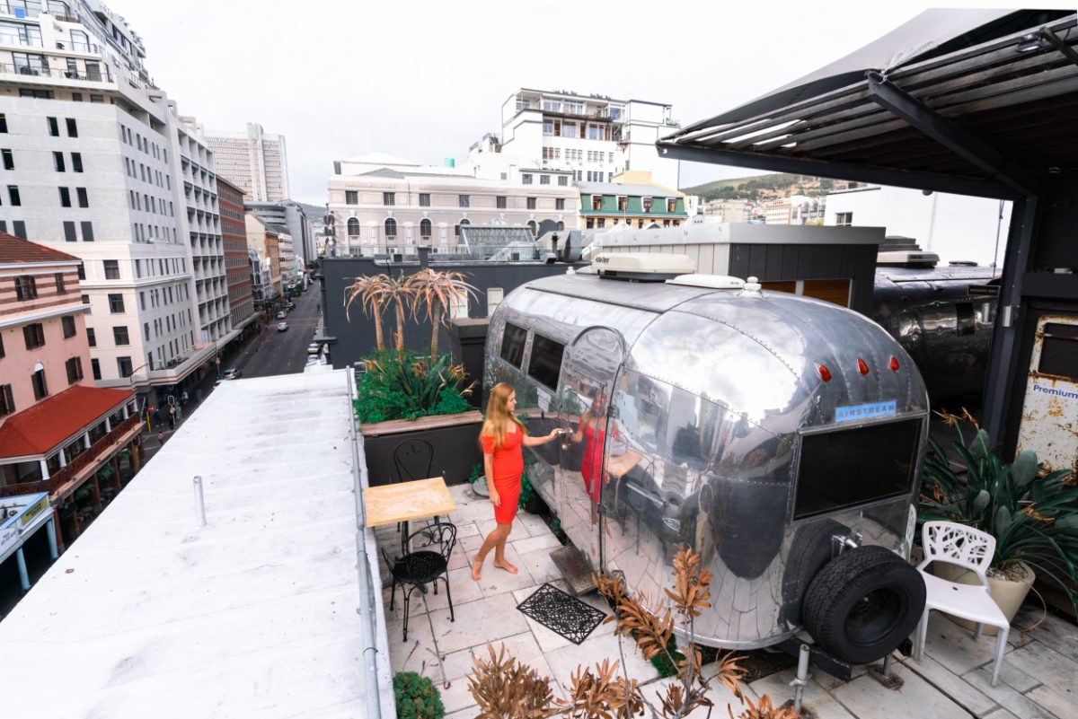 Woman opening an Airstream trailer on a rooftop in Cape Town, part of an unconventional urban accommodation experience, perfect for travelers looking for unusual stays.