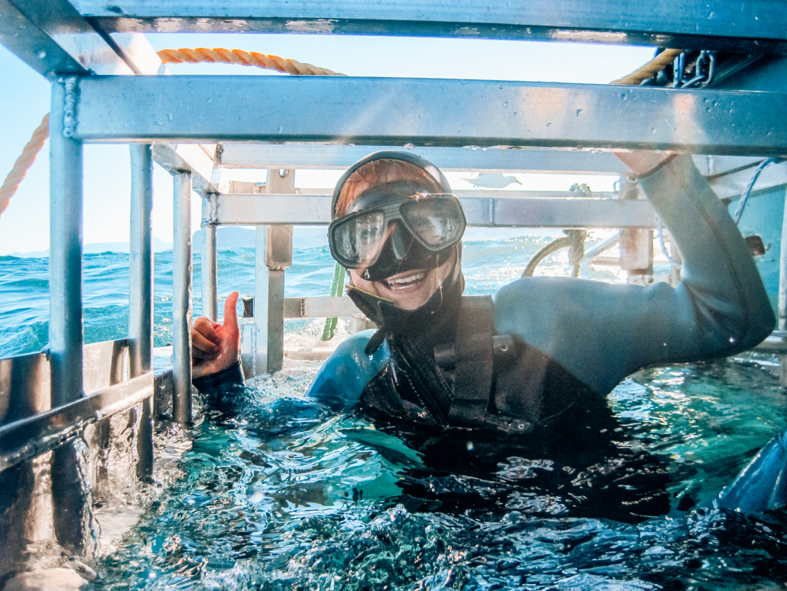 Adventurous diver giving a thumbs up in a shark cage diving experience near Cape Town, an activity that offers an up-close encounter with the marine life of South Africa.