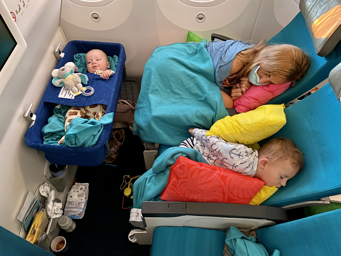 Baby resting in an airplane bassinet with a sibling asleep next to them, highlighting the difference between a car seat vs bassinet