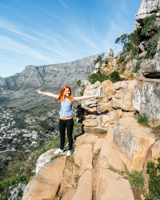 Hiker on Lions Head with arms outstretched, facing the city of Cape Town, capturing the sense of adventure and freedom tourists can experience in the city