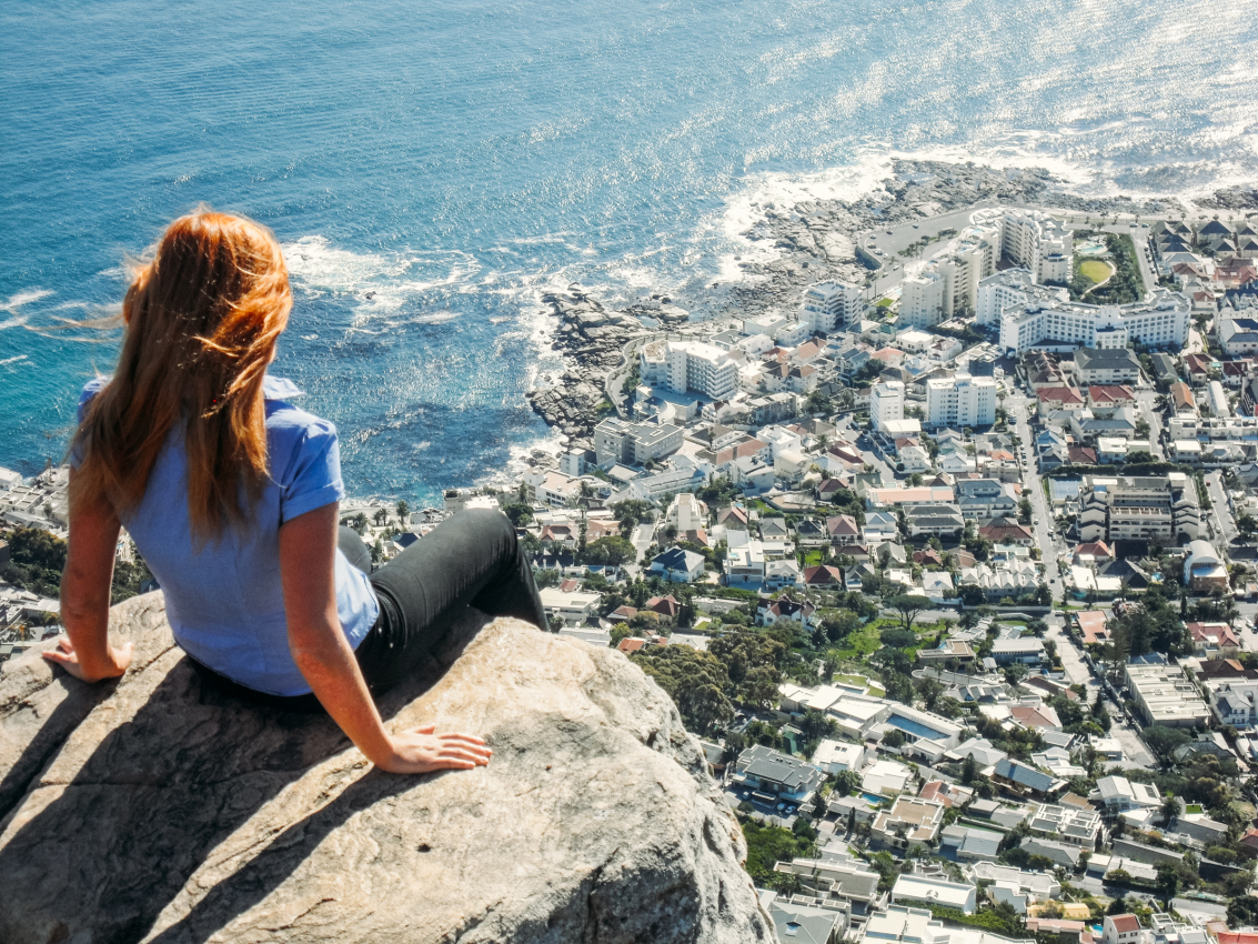 Woman gazing over the seaside cityscape of Cape Town from the summit of Lions Head, enjoying one of the best panoramic views the city has to offer.