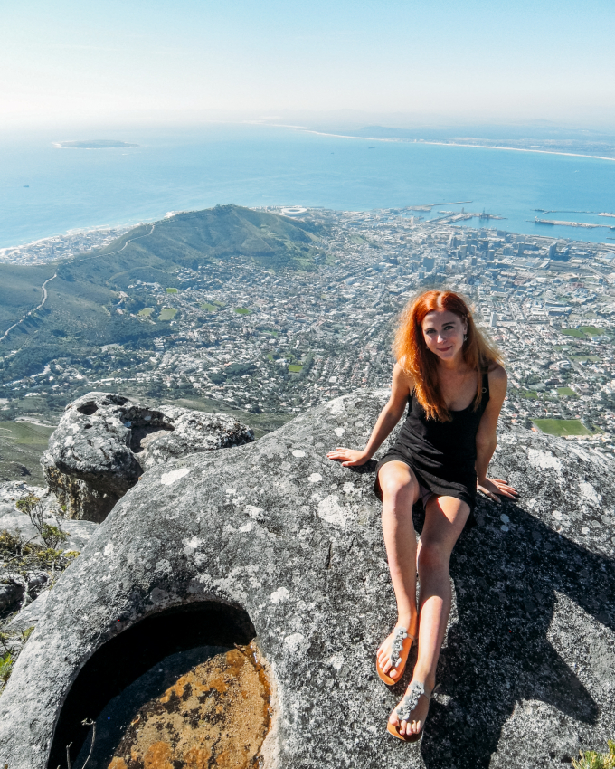 Tourist sitting atop Table Mountain with a spectacular view of Cape Town's cityscape below, a must-do for adventurous travelers visiting Cape Town.