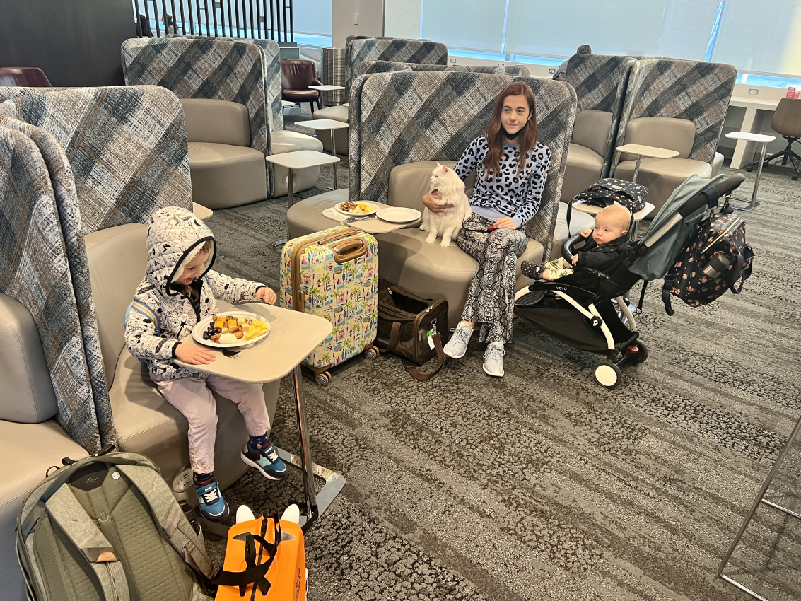 Family in a lounge area with a toddler enjoying a meal at a small table, while a woman with a cat on her lap sits near a baby in a stroller, highlighting traveling in France with a baby.
