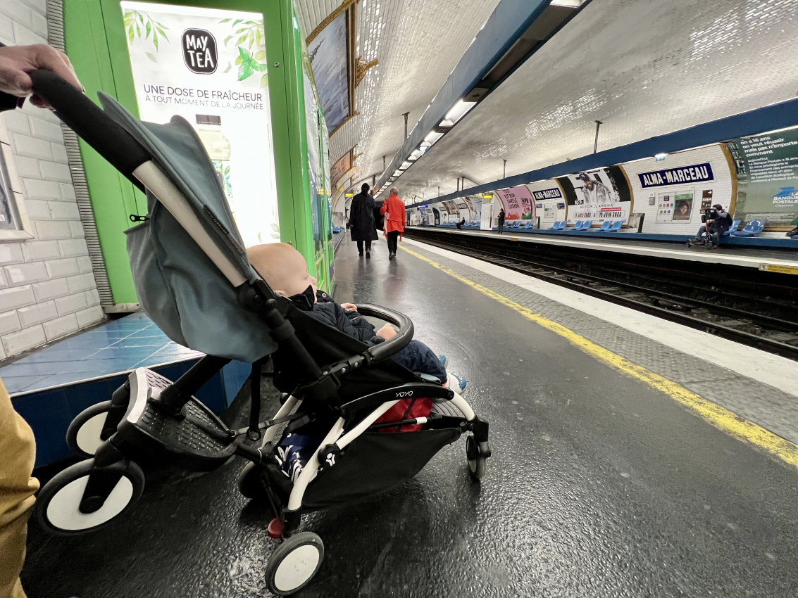 A baby in a stroller waits at a Paris metro station, representing the convenience of public transport in France with a baby.