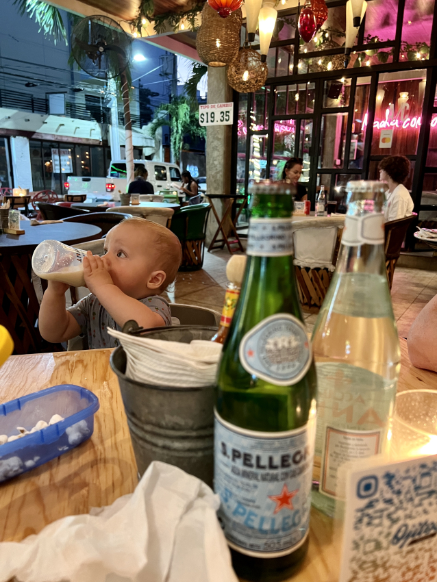 Baby bottle-feeding under the glow of festive lights at a Mexican restaurant, a family-friendly dining experience.
