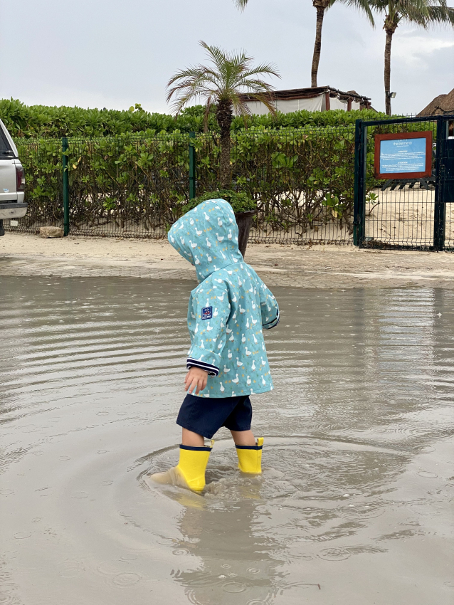 Little adventurer in a blue raincoat splashing in puddles, enjoying a rainy Mexican day with bright yellow boots.