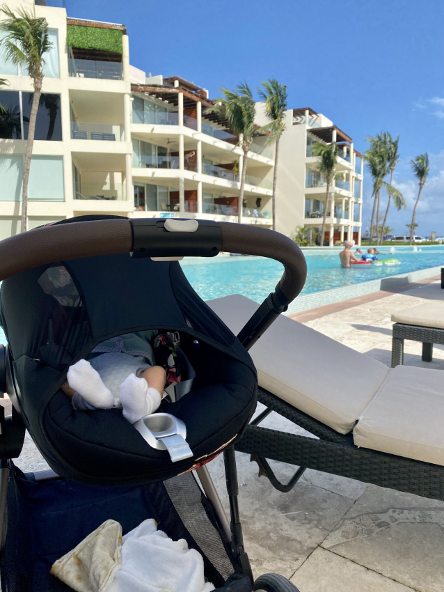 Baby sleeping peacefully in a stroller by the pool in Mexico, embodying the ease of vacationing with a baby.