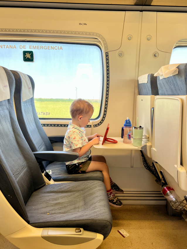 A young toddler focused on coloring, seated at a table on a train, a common scene when traveling through Spain with kids.
