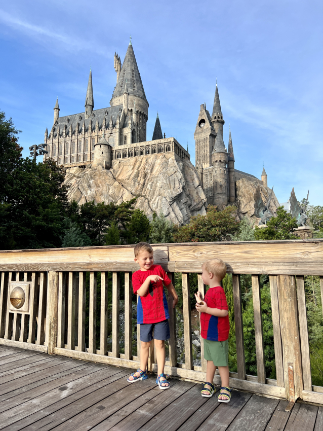 Two toddlers in red shirts laughing together on a wooden bridge with the iconic castle at Universal Studios Orlando in the background, a perfect setting for families with toddlers.
