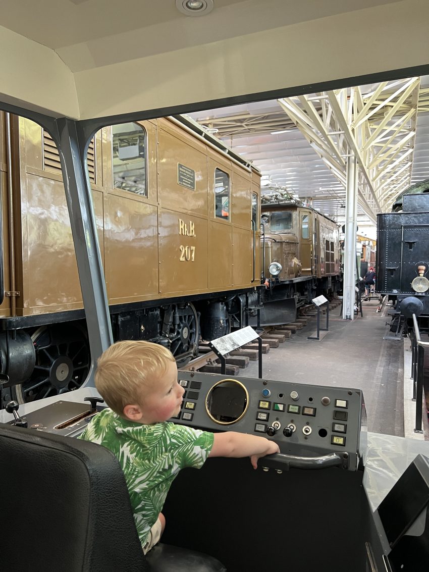 Little child playing train conductor at a Swiss transportation museum, a delightful experience for kids fascinated by trains.