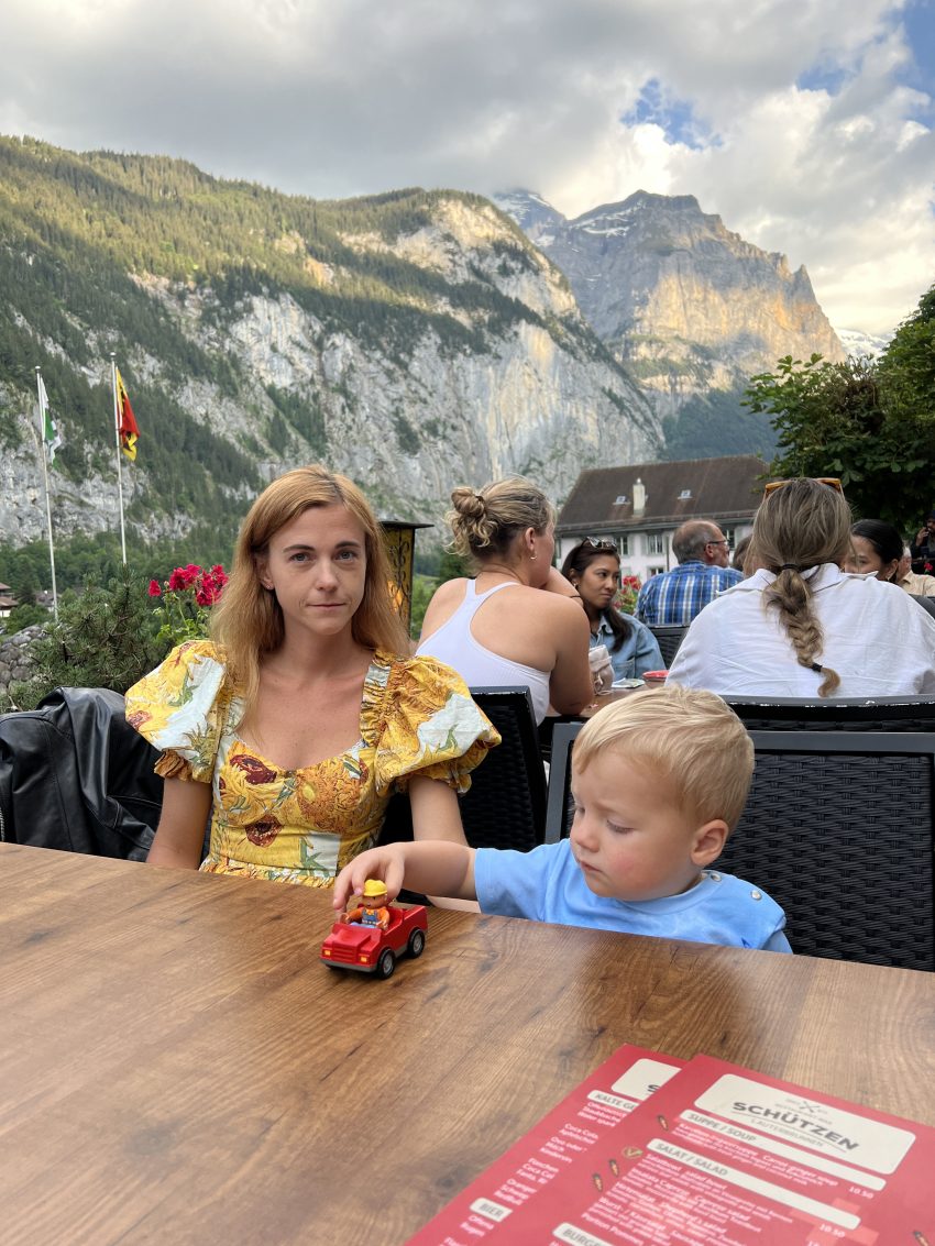 Young family dining al fresco with the majestic Swiss mountains in the background, enjoying the simplicity of a meal in Switzerland with kids.
