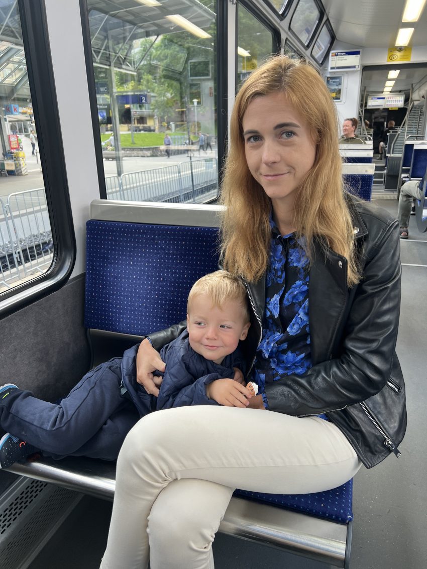 Woman with a child in her lap on a public tram, a moment of rest during their family-friendly exploration of Switzerland.
