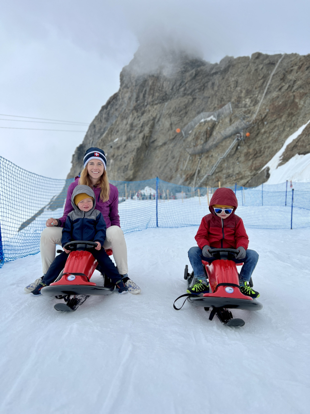 Mother and children sledding on a snow-covered slope, a joyful activity for families traveling in Switzerland with kids.
