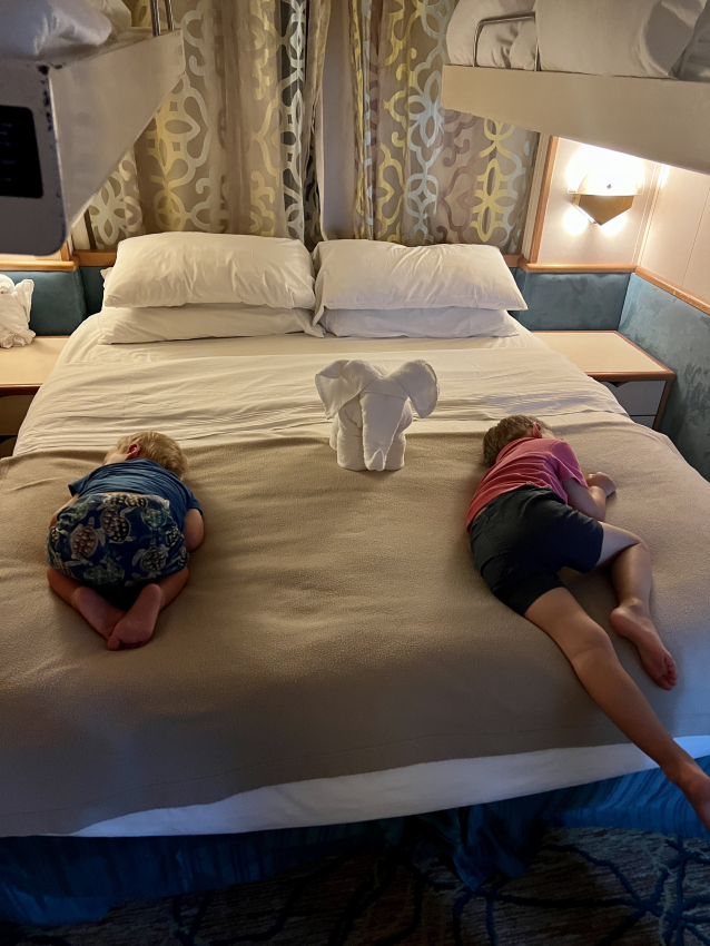 Kids napping on a large bed in a cruise ship cabin, a peaceful moment while cruising with a toddler.
