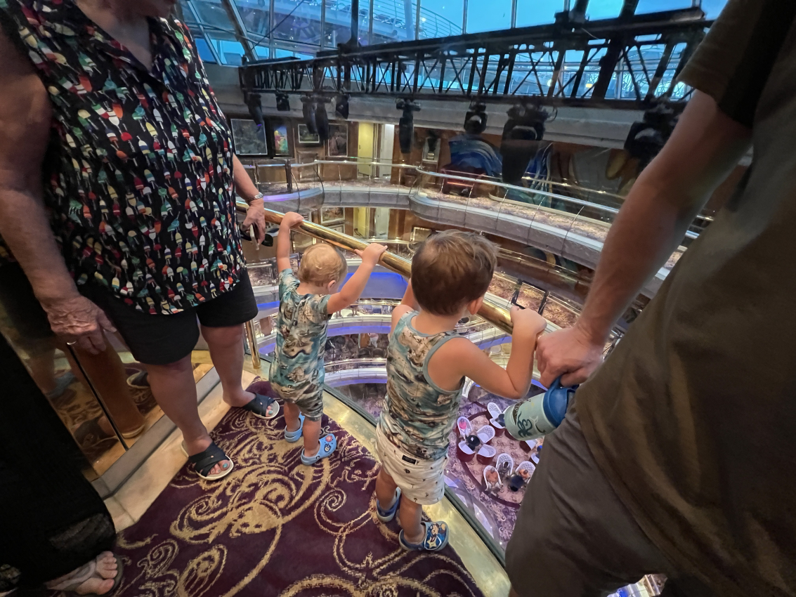 Young children looking over the interior railing of a cruise ship, a family adventure while cruising with a toddler.
