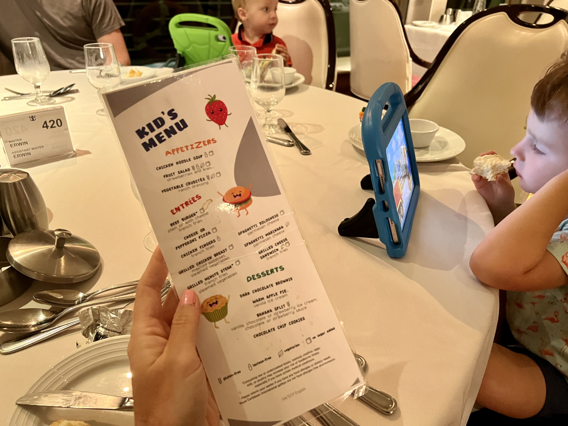 Kid's menu in focus with a child entertained by a tablet, dining made easy while taking kids on a cruise.
