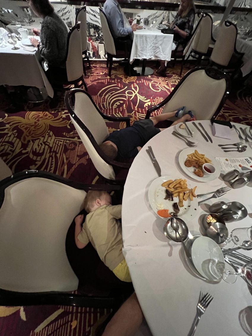 Exhausted child asleep under a table after a meal, a real moment when cruising with a toddler.
